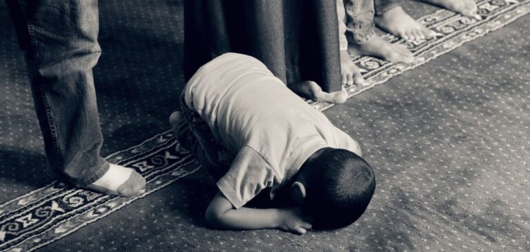 Uma foto em preto e branco, onde um menino parece rezando e parece pês de pessoas em pé, esta imagem representa o texto Intolerância religiosa