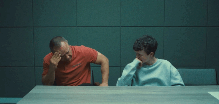O jovem e seu pai, protagonistas da série Adolescência, sentados lado a lado em uma sala de interrogatório, com expressões de angústia e cansaço.