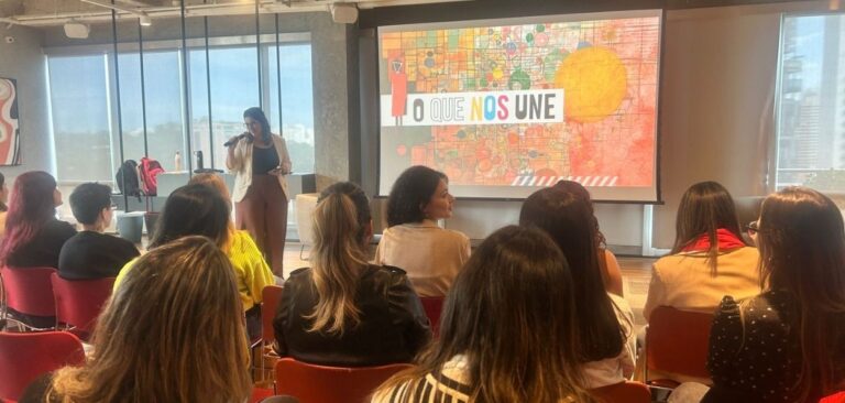 Palestra sobre diversidade em ambiente corporativo, com público atento e a frase “O que nos une” projetada na tela.