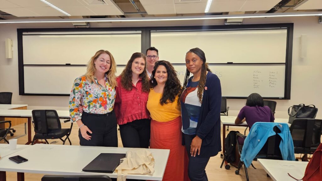 Grupo de pessoas sorrindo em sala de aula durante formação sobre sustentabilidade e impacto social. São Alunos da NCSU e a Lorena Martins de Carlotas